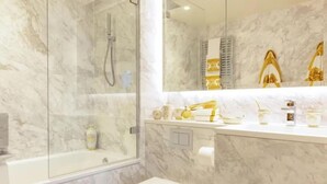 A bathroom with a glass-enclosed shower, marble walls, and a vanity with toiletries.