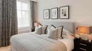 A modern hotel bedroom with a large bed, grey curtains, and three framed pictures on the wall.