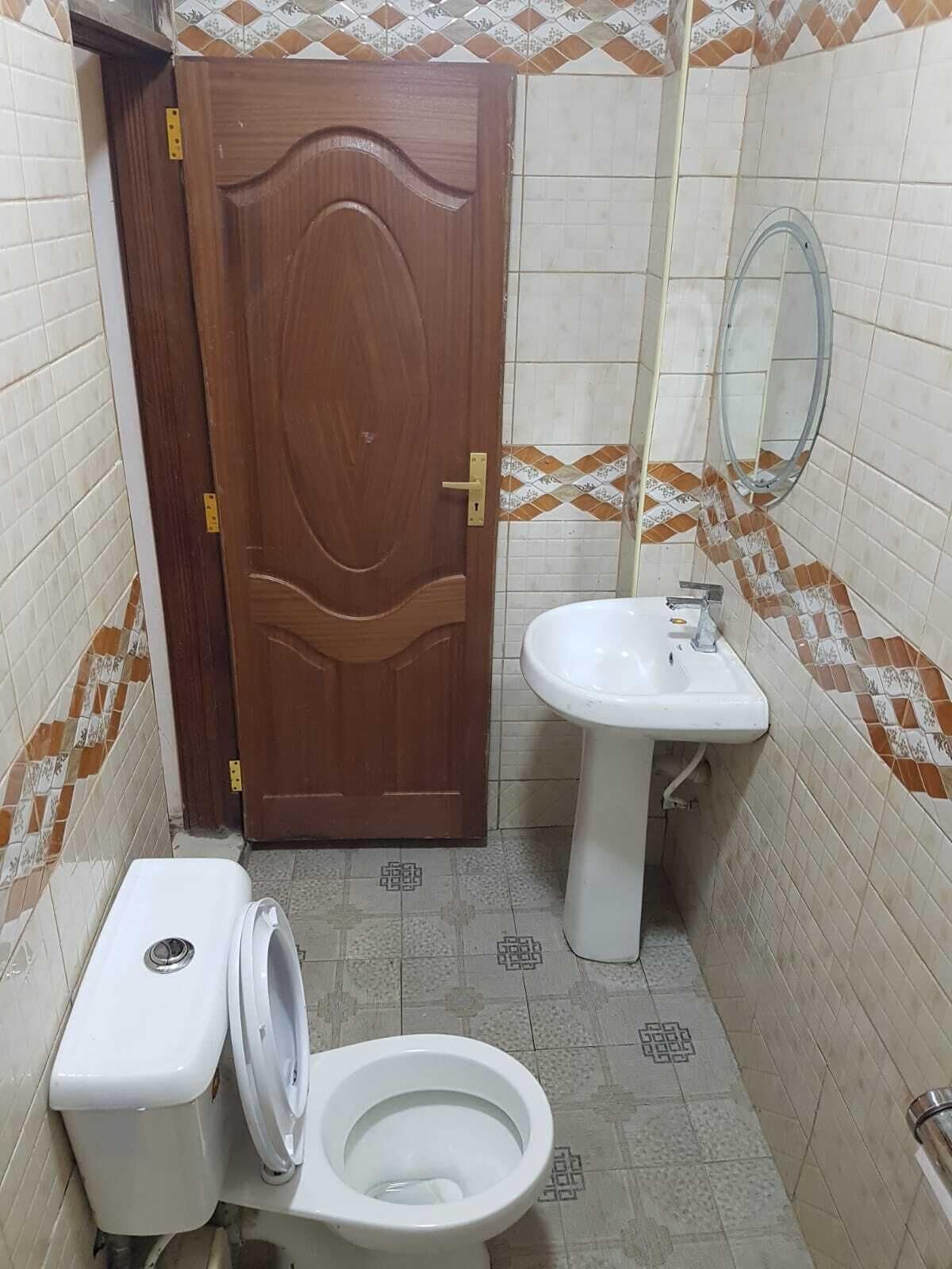 Un baño pequeño con puerta de madera, un inodoro, un lavabo y un espejo.