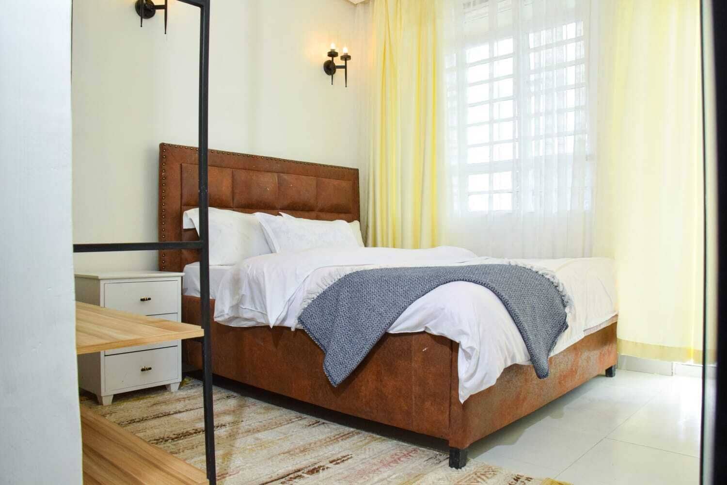 A bedroom with a wooden bed, white bedding, a bedside table, and a mirror.