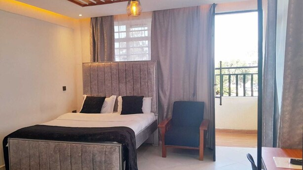 A bedroom with a bed, a chair, a table, and a balcony. - Sandalwood Suites Nakuru (Nakuru)