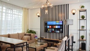 A modern living room with a sofa, coffee table, and chairs. There is a television mounted on the wall displaying various channels. - Sandalwood Suites Nakuru (Nakuru)