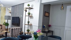 A modern living room with a glass dining table, blue chairs, a sofa, and a TV. - Sandalwood Suites Nakuru (Nakuru)