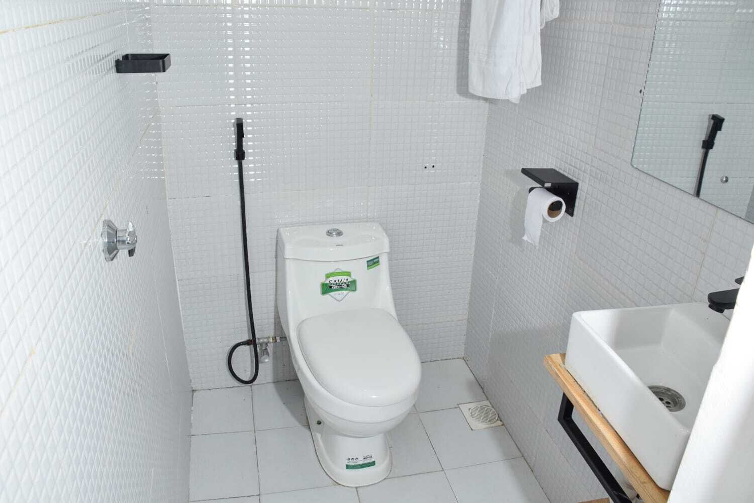 A small, white tiled bathroom with a toilet, a bidet, and a sink.