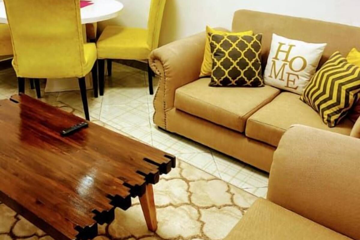 Una sala de estar con un sofá color beige, sillas amarillas, una mesa de centro de madera y cojines estampados.