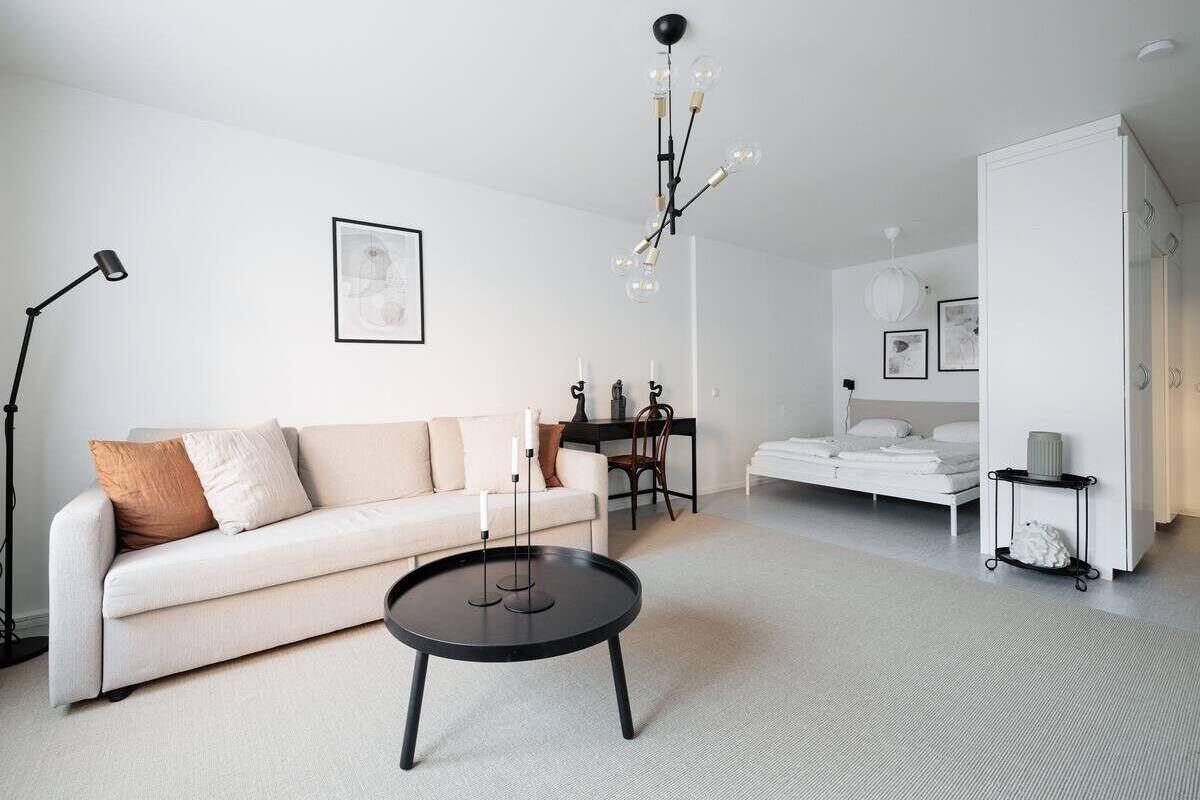 A modern living room with a sofa, coffee table, and a bed in the background.