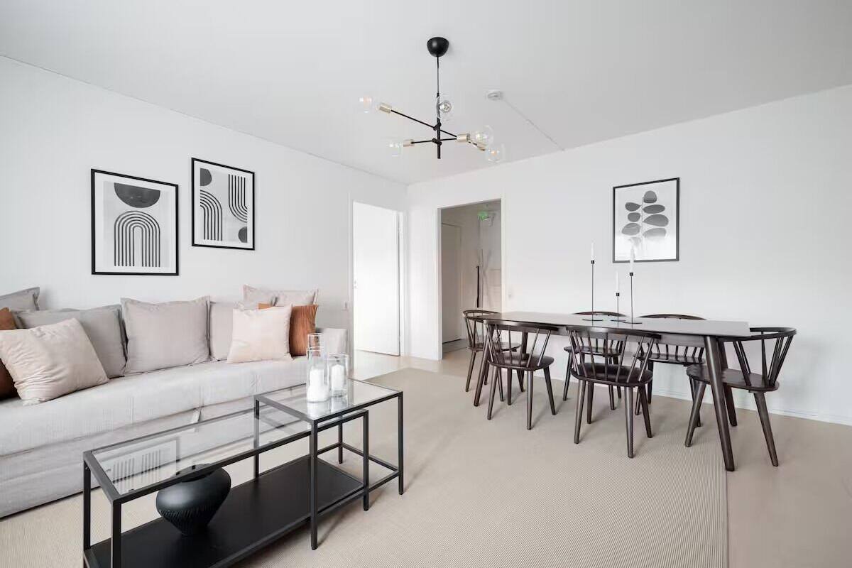 A modern living room with a white sofa, a glass coffee table, and a dining area with a round table and chairs.