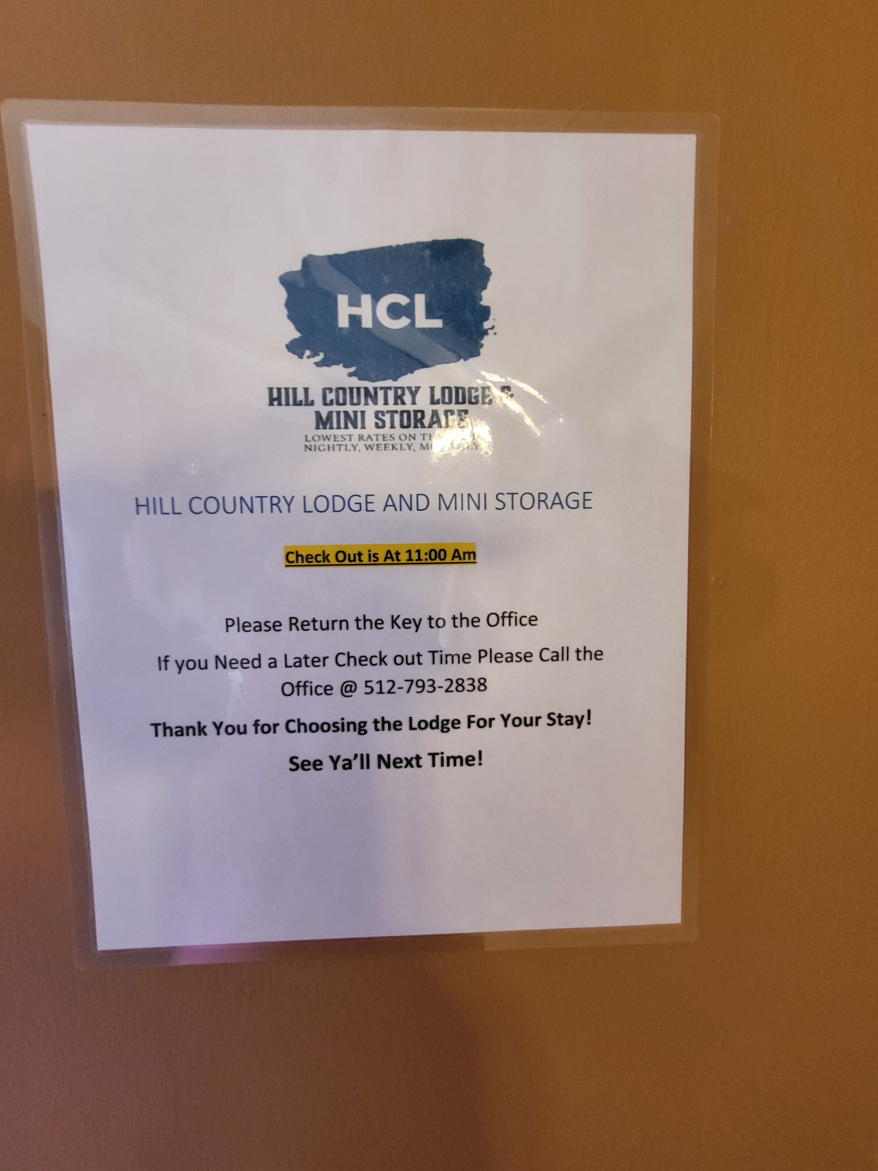 A sign for Hill Country Lodge Mini Storage with check-out time at 11:00 AM, a key return instruction, and a contact number for further inquiries.