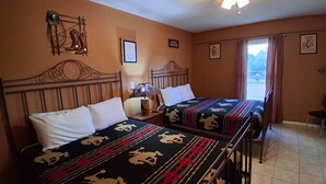 A hotel room with two beds, a wooden headboard, a nightstand, a lamp, a framed picture, a window with curtains, and a ceiling fan.