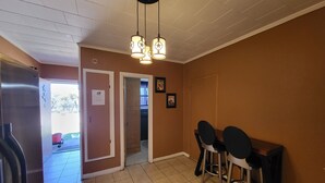 A hallway with a refrigerator, a door leading to a bathroom, and a seating area with chairs and a table.
