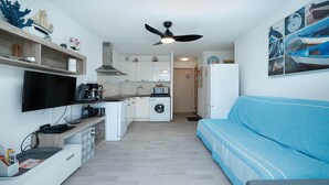 A compact living space with a kitchenette, a washing machine, a flat-screen TV, and a blue sofa. - Apartment in Agde Near Beach & Heated Pool (Agde)