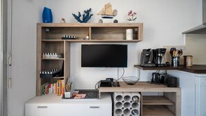 A compact living space with a TV mounted on a wooden wall, a coffee machine, and a bookshelf with various items. - Apartment in Agde Near Beach & Heated Pool (Agde)