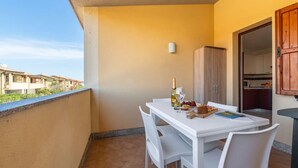 A balcony with a white table and chairs, a bottle of champagne, and a book. - Cozy Flat Just Steps From Baia Delle Mimose (Badesi)