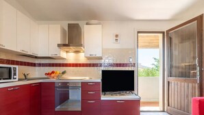 A modern kitchen with red cabinets, a microwave, a stove, and a TV. - Cozy Flat Just Steps From Baia Delle Mimose (Badesi)