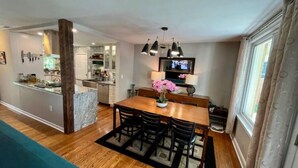 A modern kitchen with a dining area, wooden flooring, and a TV mounted above the table.
