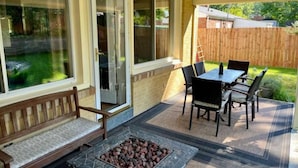 A covered patio with a stone fire pit, a wooden bench, and a table with chairs.