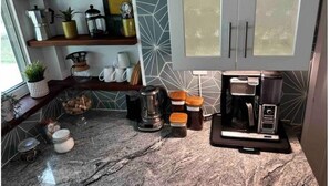 A kitchen with granite countertops, a coffee maker, jars, and a 'CRAFT' sign on the shelf.