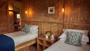 Een houten kamer met twee bedden, een kleine tafel met een bloemenvaas en een foto aan de muur.