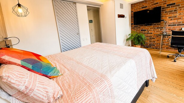 A bedroom with a bed, a television, a plant, and a sliding door.