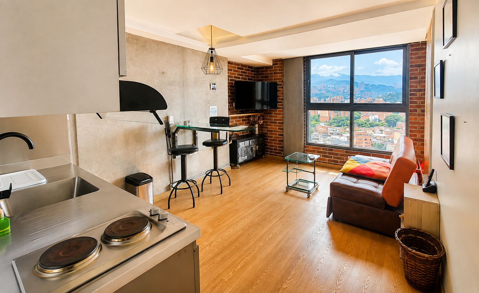 A modern kitchen with a dining area, a sofa, and a large window with a city view.