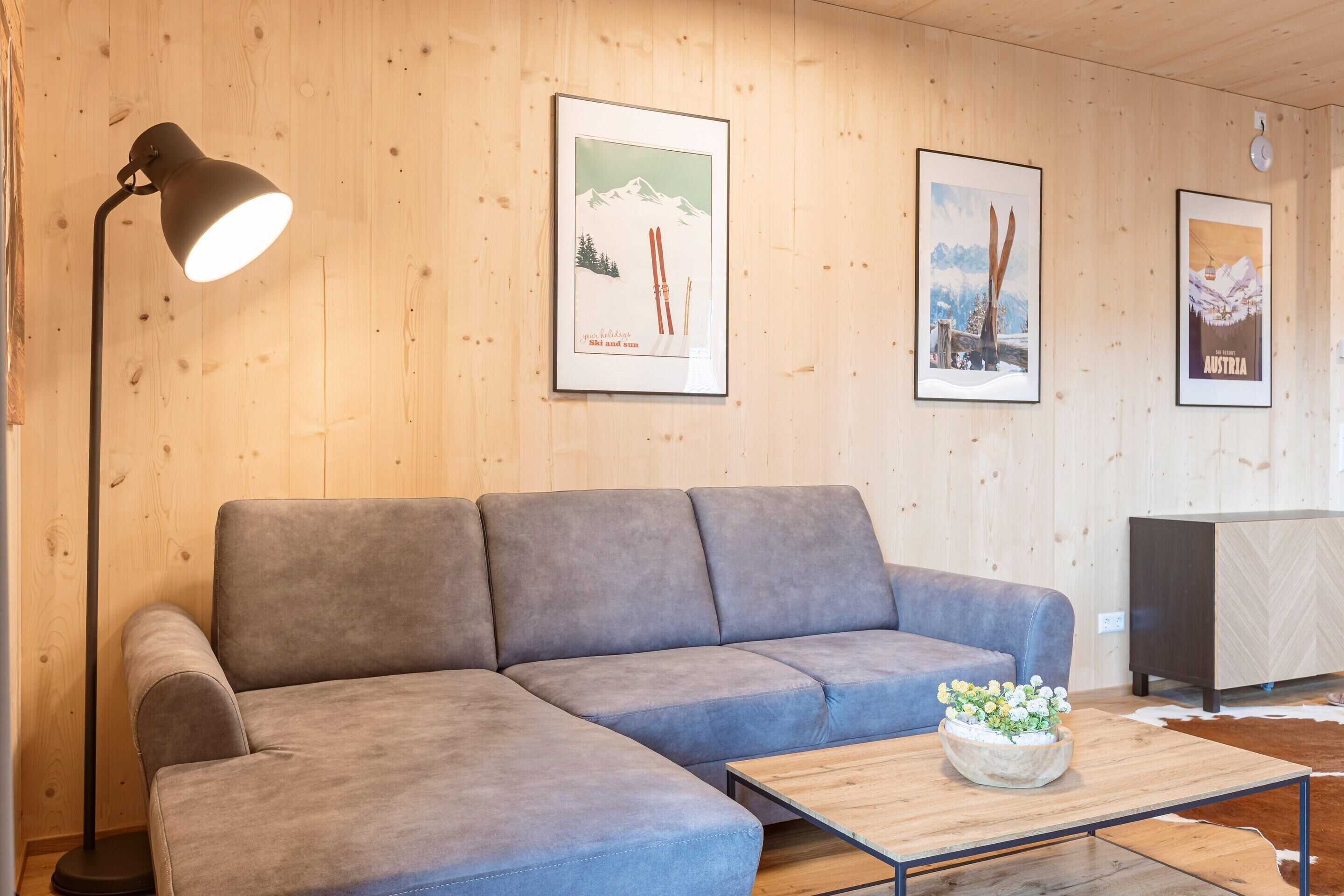 En moderne stue med en grå hjørnesofa, et træ sofabord med en vase og billeder i rammer på væggen.