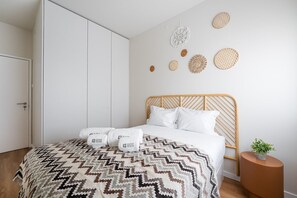 A bedroom with a bed, a wardrobe, a bedside table with a plant, and decorative wall art.