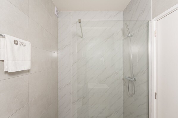 A modern shower with a glass door, a towel rack with a towel, and a marble-patterned wall.