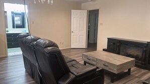 A living room with a leather sofa, a wooden coffee table, a fireplace, and a chandelier. - Reserved Luxury (Lubbock)