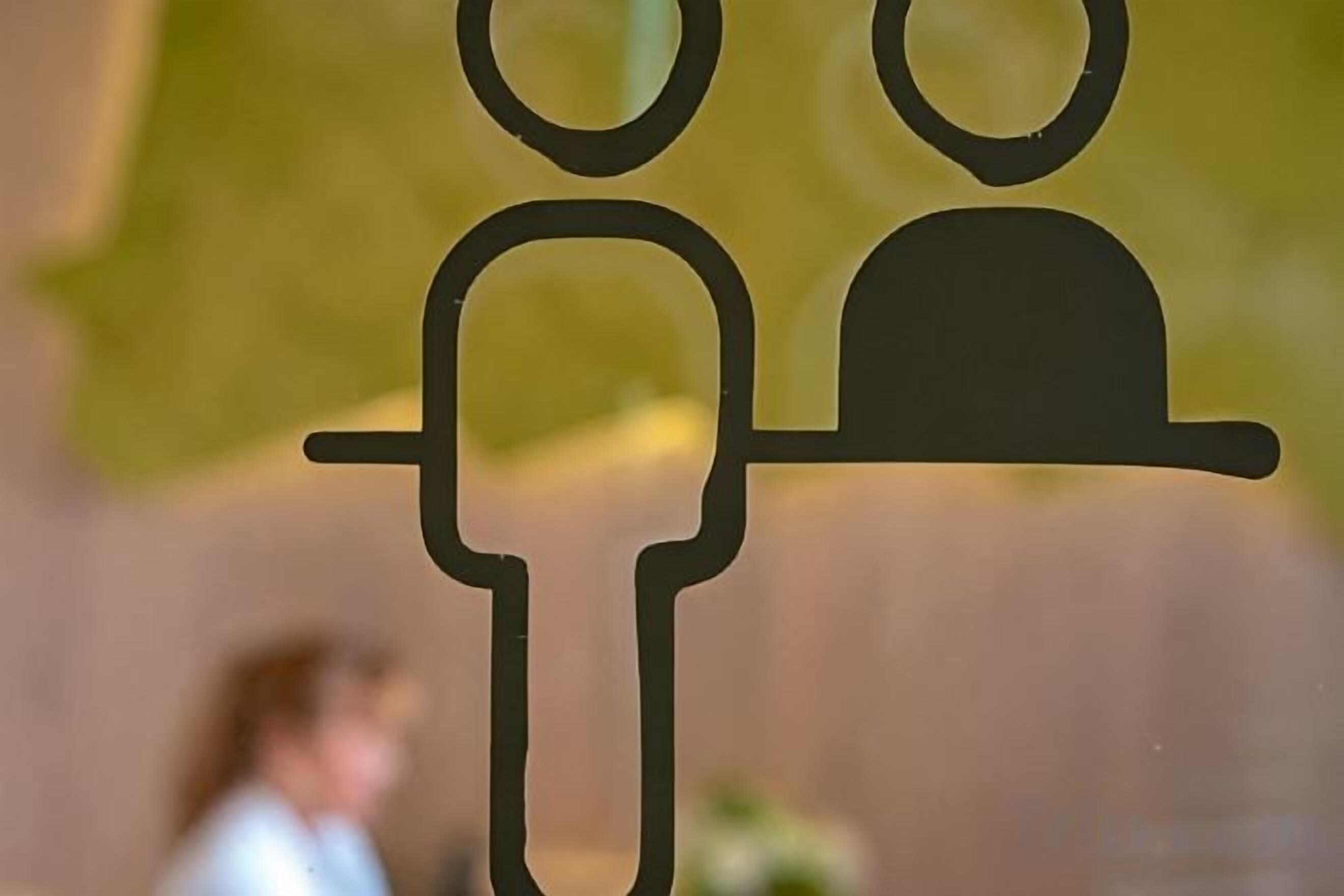 A silhouette of a person with a hat, possibly a waiter or server, against a blurred background.
