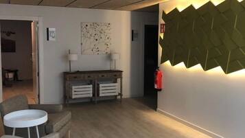 A modern interior with a wooden floor, a white round table, a sofa, a cabinet with drawers, and a wall-mounted light fixture.