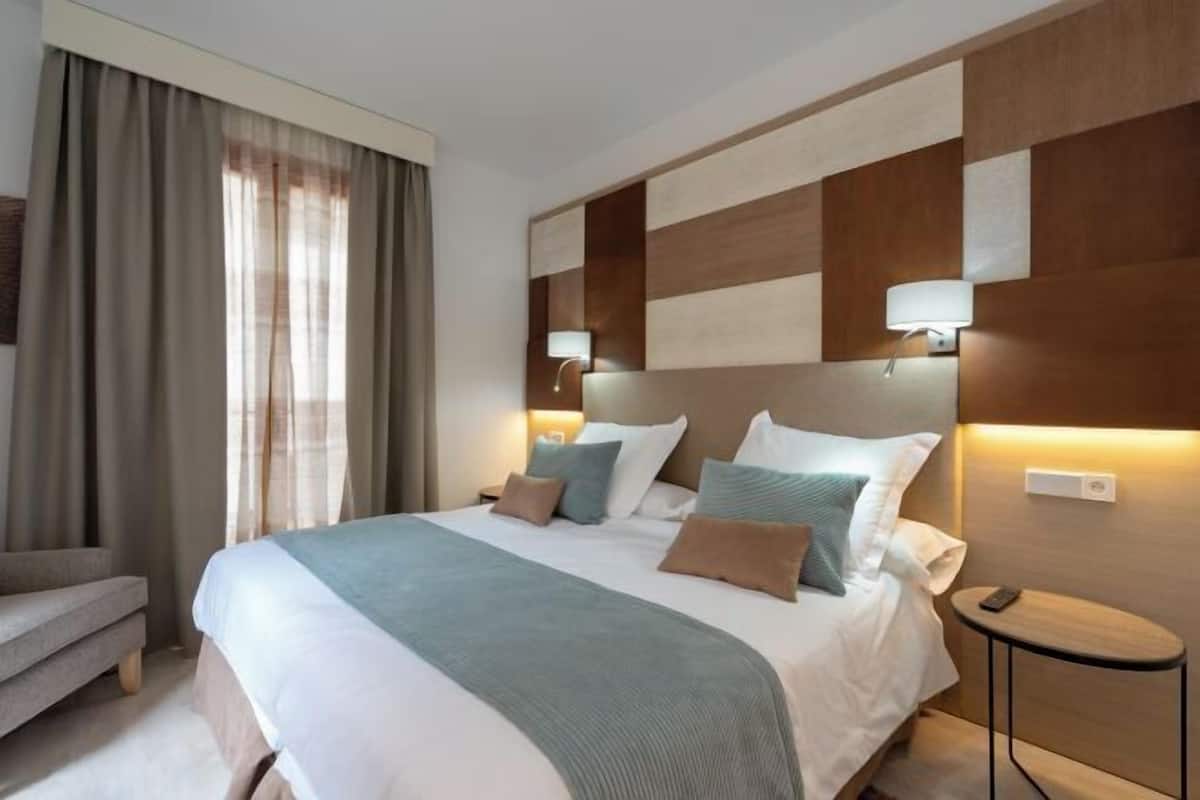 A hotel room with a large bed, bedside lamps, a small table, and a chair.