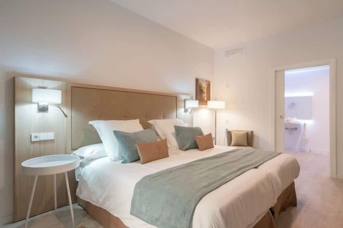 A hotel room with a large bed, bedside lamps, a small table, and a door leading to a bathroom.