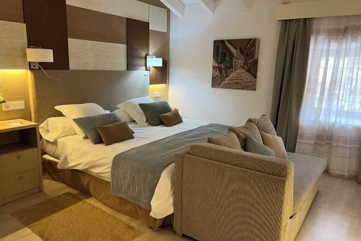 A modern hotel room with a large bed, a sofa, a desk, and a painting on the wall.