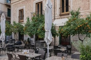 An outdoor cafe with tables and chairs, umbrellas, and orange trees. - Soller Plaza (Soller)