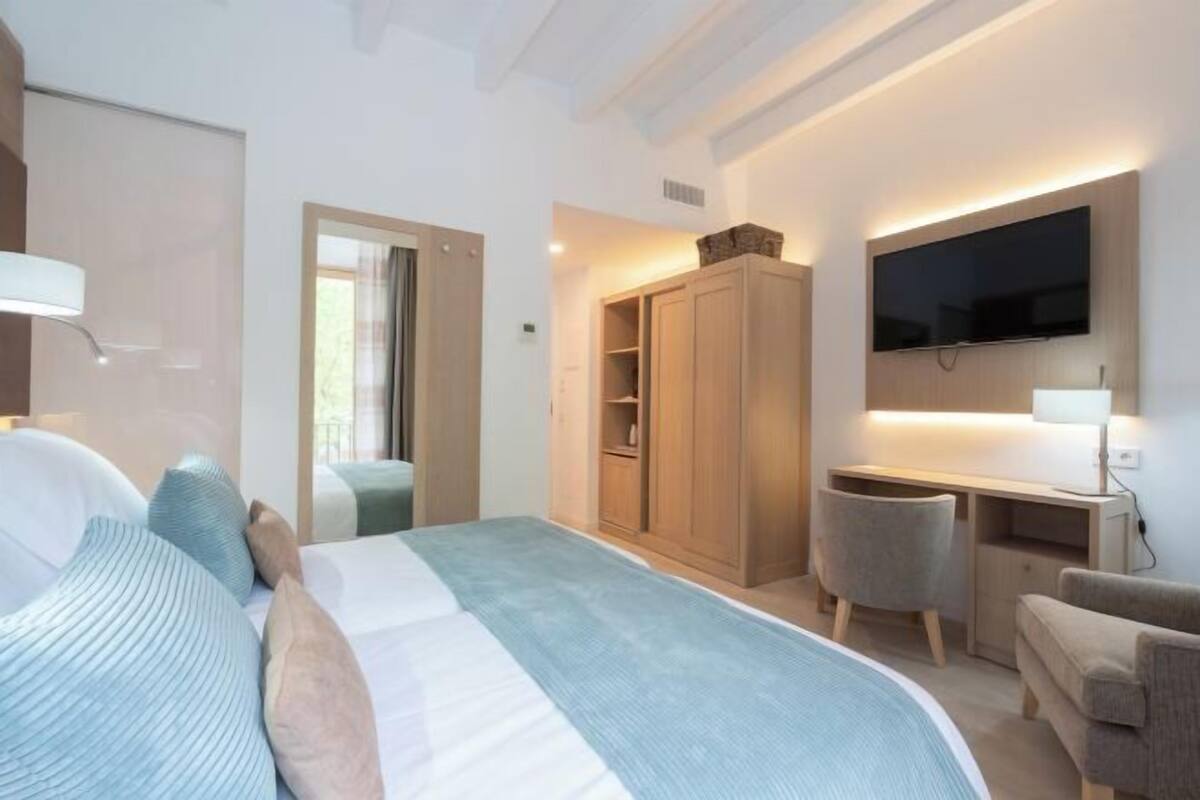 A modern bedroom with a bed, wardrobe, desk, and TV.