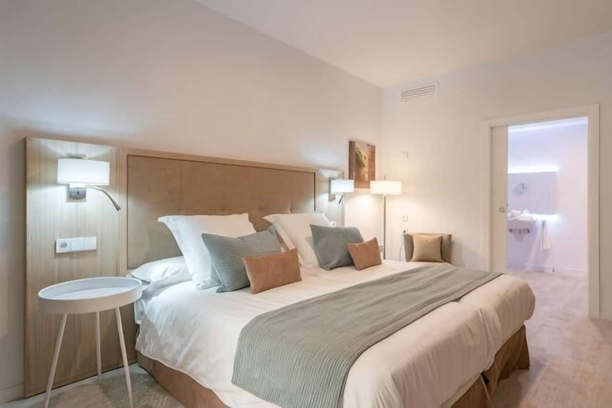 A hotel room with a bed, bedside lamps, a small round table, and a door leading to a bathroom.
