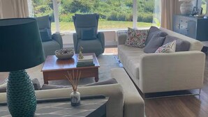 Un salon comprenant un canapé, des fauteuils, une table basse et offrant une vue sur la verdure et les montagnes.