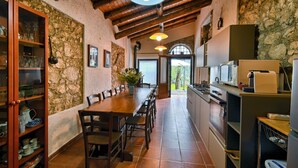 Une cuisine rustique avec une table à manger en bois, des murs en pierre et une arche en pierre qui mène à l’extérieur.