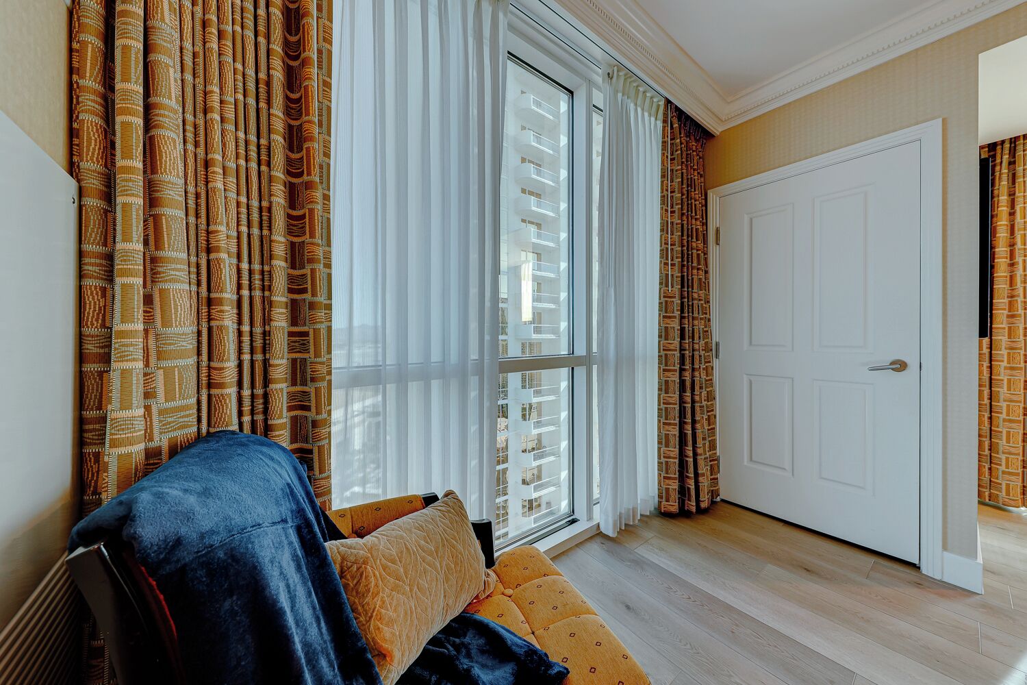 A room with a sofa, patterned curtains, a large window, and a white door.