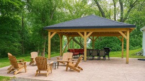 Eine überdachte Terrasse mit Adirondack-Stühlen, einem roten Sofa und einem Grill.