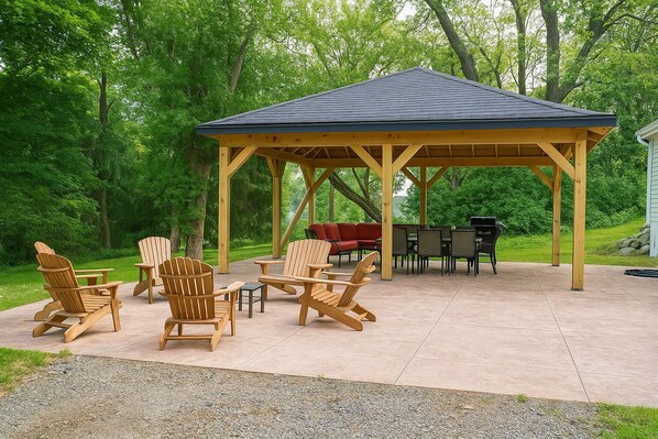 Une terrasse extérieure couverte, aménagée avec des fauteuils Adirondack, un canapé rouge et un barbecue.