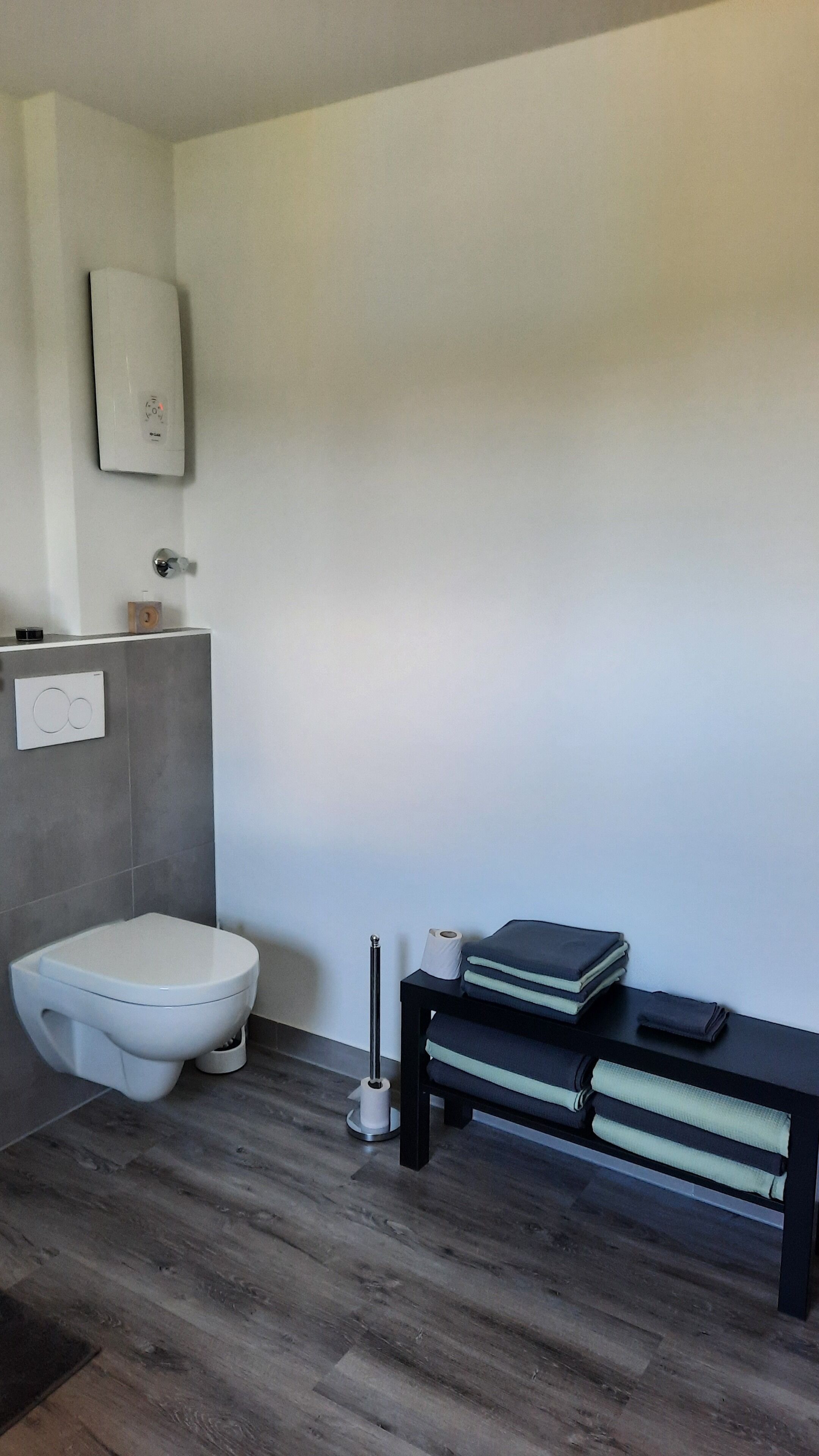 Une salle de bain moderne équipée de toilettes, d’un porte-serviettes et d’une petite étagère contenant des articles de toilette.