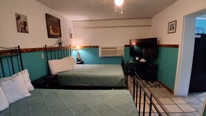 Une chambre avec deux lits, un ventilateur de plafond, une télévision et une petite table avec une lampe.