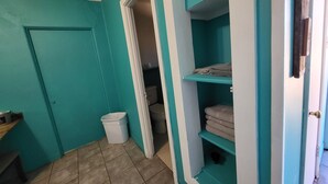 Une salle de bain aux murs de couleur turquoise, avec des toilettes, un lavabo et une étagère où sont pliées des serviettes.