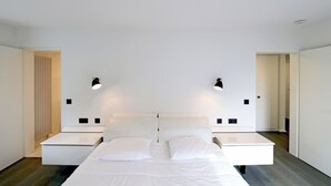 A modern bedroom with a large bed, two bedside tables, and two wall-mounted lamps. - Apartment in Het Zoute With Sea Views (Knokke-Heist)