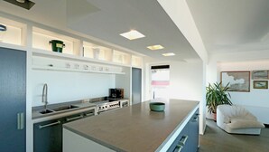 A modern kitchen with a central island, built-in appliances, and a dining area with a chair and a plant. - Apartment in Het Zoute With Sea Views (Knokke-Heist)