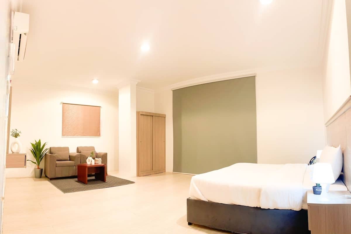 Ein modernes Schlafzimmer mit einem großen Bett, einer kleinen Sitzecke mit Tisch und einer Wand in Grünton.