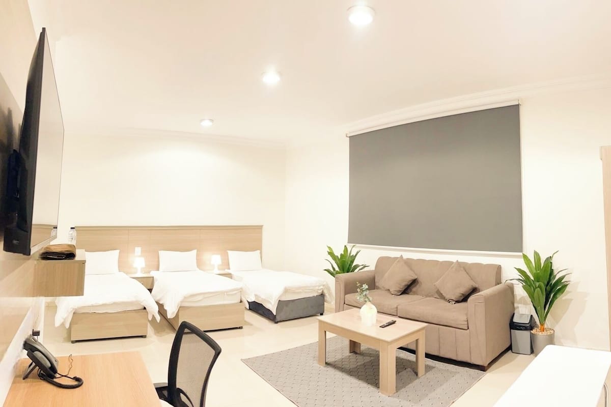 Ein modernes Hotelzimmer mit einem großen Bett, einer Couch, einem Couchtisch, einem Schreibtisch mit Telefon und einem Fernseher.