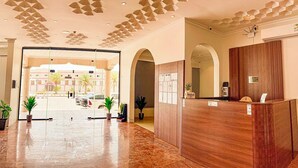 Zona de recepción de un hotel con un mostrador de madera, una puerta de cristal y un techo con diseños geométricos.