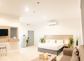 Ein modernes Hotelzimmer mit Bett, Fernseher, Küchenzeile und einer Sitzecke.